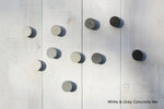 Wooden panelled whitewashed wall with circular concrete hooks in white and gray. Concrete cabinet knobs in various shades of grey.
